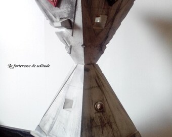 Könnte beinhalten: Eine weiße, graue und schwarze abstrakte Skulptur mit einem pyramidenförmigen Sockel und einem dreieckigen Oberteil. Die Skulptur hat eine strukturierte Oberfläche und ein kleines, rundes, metallisches Detail auf der Vorderseite. Der Text "la forteresse de solitude" ist am unteren Rand des Bildes sichtbar.