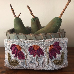 Puede incluir: Una cesta de madera rústica llena de tres peras de tela, cada una con un tallo de rama. La cesta está decorada con una alfombra cosida a mano con un diseño floral en tonos de morado, naranja y verde.