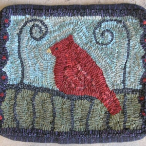 May include: A red cardinal bird perched on a green fence with blue and white swirls in the background. The image is a rug hooking, a type of craft where yarn is hooked through a woven base.