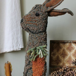 May include: A handcrafted, textured rabbit sculpture with a carrot design. The rabbit is primarily brown and green, with a large orange carrot on its body. The ears have brown accents. The sculpture is a decorative item.