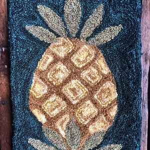 May include: A close-up of a pineapple rug with a brown and yellow pineapple on a dark blue background.