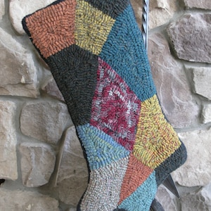 May include: A colorful patchwork stocking with a diamond pattern in shades of red, blue, yellow, and orange. The stocking is hanging on a metal hook.