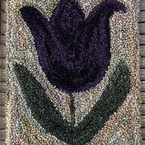 May include: A purple tulip with green leaves and a brown stem is depicted in a rug hooking style. The background is a light beige with hints of pink and green.