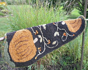 May include: A brown and black rug with a design of pumpkins and vines. The rug is made of wool and has a hand-woven texture.