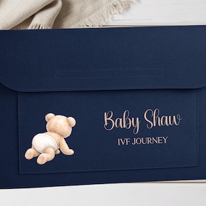 May include: A navy blue baby shower invitation featuring a watercolour illustration of a teddy bear in a nappy. The text "Baby Shower" and "IVF JOURNEY" are in a script font.