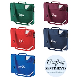 May include: A selection of personalised school satchels in green, burgundy, red, navy blue, and royal blue. Each satchel has a name printed on it in a cursive font. The satchels have a handle, a shoulder strap, and a reflective stripe.