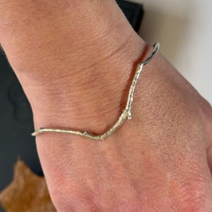 May include: A silver bracelet shaped like a branch with a delicate, twig-like design.