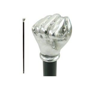 Puede incluir: Un bastón de paseo de color plateado con un mango en forma de puño detallado. El bastón es negro y tiene una punta plateada.