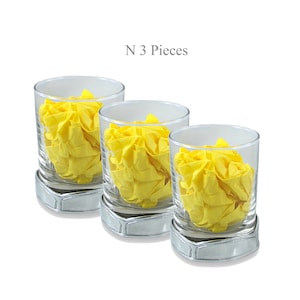 May include: Set of three clear glass tumblers with silver bases. Each tumbler contains a crumpled yellow paper napkin.