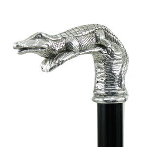 Peut inclure: Une poignée de canne en argent en forme d'alligator avec un manche en bois noir. L'alligator est sculpté dans une pose réaliste, la tête levée et la queue enroulée autour du manche.