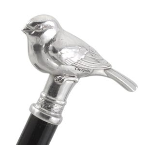 Op de afbeelding: Een zilverkleurig metalen vogelbeeldje gemonteerd op de handgreep van een zwarte wandelstok. De vogel heeft gedetailleerde vleugel- en vederstructuren, met het woord Cavagnini aan de zijkant gegraveerd. De handgreep heeft een decoratieve zilveren kraag.