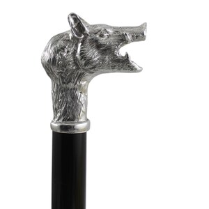 Könnte beinhalten: Ein Gehstock mit einem silberfarbenen Metallgriff in Form eines detaillierten Wildschweinkopfes mit offenem Maul und sichtbaren Hauern. Der Griff ist an einem glatten, massiven schwarzen zylindrischen Schaft befestigt, was einen deutlichen Kontrast zwischen dem metallischen Tierkopf und dem dunklen, geraden Körper des Stocks erzeugt.