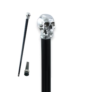 Op de afbeelding: Een zwarte wandelstok met een zilveren schedelkop. De schedel heeft gedetailleerde gelaatstrekken en zit bovenop een zwarte schacht. De stok heeft ook een rubberen tip en een zilveren kraag.