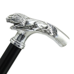 Peut inclure: Une canne de marche dotée d'une poignée en métal argenté poli en forme de lion accroupi avec une crinière détaillée. La poignée est fixée à un bâton noir lisse et solide. La poignée métallique porte l'inscription gravée "MADE IN ITALY".