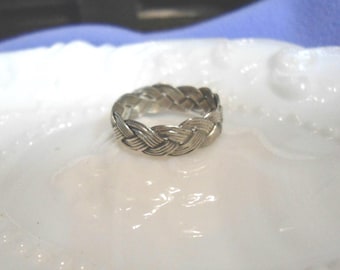 May include: A silver-toned ring featuring a continuous braided or woven metal pattern around the entire band. The surface of the ring displays a textured, multi-strand design that mimics the appearance of a plait, creating a uniform metallic finish.