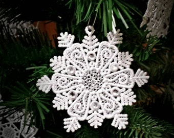 May include: White lace snowflake ornament hanging on a green artificial Christmas tree.