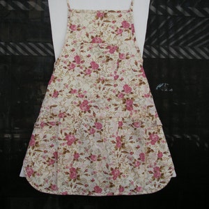 May include: A white apron with a floral pattern in shades of pink and brown. The apron has a large pocket on the front and adjustable straps.