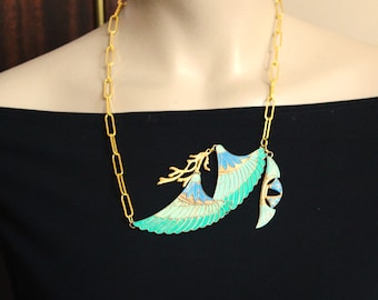 May include: A gold chain necklace with a large pendant featuring a stylised turquoise and blue bird wing design.