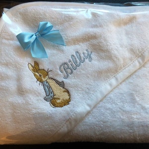 Peut inclure: Serviette à capuche blanche avec un ruban bleu et un lapin de Pâques brodé ainsi que le nom "Billy"