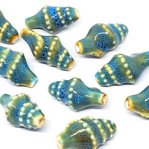 May include: Ten ceramic beads in a blue, green and white speckled pattern. The beads are shaped like a seashell and have a hole in the centre for stringing.