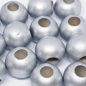 May include: Close-up of several silver-painted wooden beads. Each bead is round with a large, centered hole. The beads have a metallic sheen and a smooth, slightly irregular surface, suggesting they are handmade.