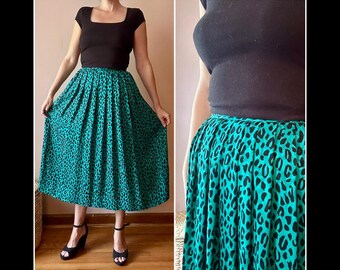 May include: A teal and black leopard print skirt with a high waist. The skirt is paired with a black top and black wedge sandals. The skirt is a midi length and has a full, pleated design.
