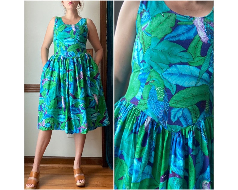 Op de afbeelding: Een blauwe en groene jurk met bloemenprint, een getailleerd bovenstuk en een volle rok. De jurk heeft een ronde halslijn en is mouwloos.