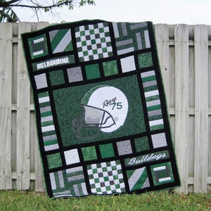 May include: A green and black quilt featuring a football helmet design in the centre. The quilt incorporates a variety of patterns, including stripes, chequered, and solid colours. The text "Ray 75" and "Bulldogs" are visible on the quilt.