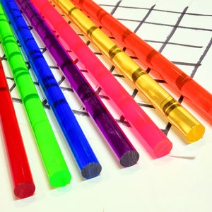 May include: Seven colorful acrylic rods with a striped pattern. The rods are arranged in a fan shape on a white surface with a black grid pattern.