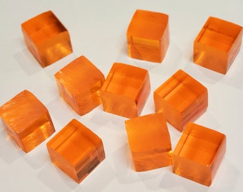 May include: Ten small, translucent orange cubes made of glass or plastic. The cubes are scattered on a white surface.