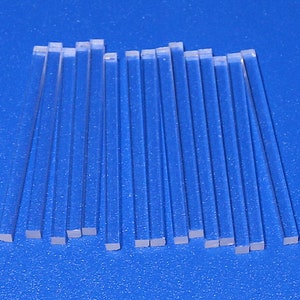 May include: A group of 20 clear acrylic rods, all the same size, laid out on a blue surface.