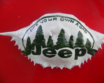 Green and white "Make your own road" Jeep pine trees painted on crab shell ornament. Packaged in a plastic container with coordinated shred