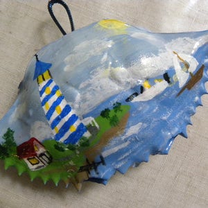 Blue and white lighthouse with seaside  scenery painted on crab shell ornament.  Comes in plastic container ready to wrapnt.