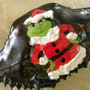The Grinch hands on hips black background  painted crab shell ornament. Packaged in a plastic container with coordinated shred