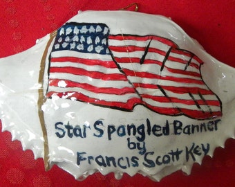 The Star Spangled Banner written by Francis Scott Key painted crab shell ornament. Packaged in a plastic container with coordinated shred