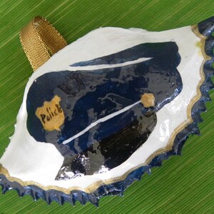 Police Hat With Police Shield Painted Crab Shell OrnamentIt comes packaged in a plastic container with coordinated shred