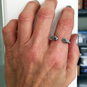 May include: A silver ring with a wing design. The ring is open and adjustable to fit different finger sizes.