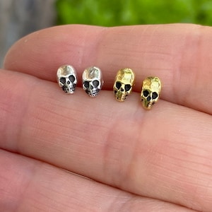 May include: Two pairs of skull stud earrings. One pair is silver and the other is gold.