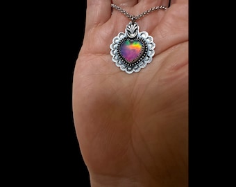 May include: A silver heart-shaped pendant necklace with a iridescent gemstone. The pendant is surrounded by a decorative silver border.