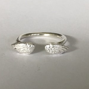 May include: A silver ring with two angel wings on either side. The wings are detailed and have a textured finish.