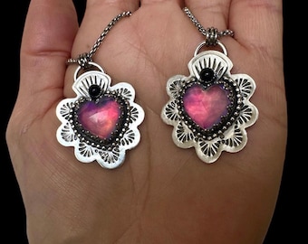 May include: Two silver heart-shaped pendants with pink and purple iridescent glass hearts and black accents. The pendants are on silver chains.