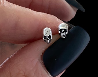 May include: A pair of silver skull stud earrings. The earrings are small and delicate, and they feature a detailed skull design.