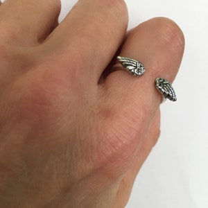 May include: A silver ring with two angel wings on the band. The wings are detailed and have a textured finish.