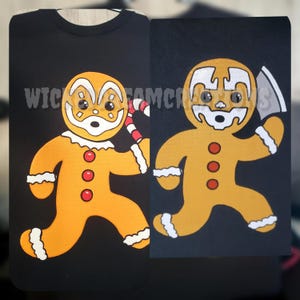 May include: Black t-shirts with a gingerbread man graphic. One gingerbread man holds a candy cane, the other holds a cleaver. The gingerbread men are orange with white and red accents. The text "Wick Fam Clicks" is visible.