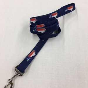 Op de afbeelding: Een blauwe hondenriem met een herhalend patroon van de vlag van de staat North Carolina. De riem heeft een zilveren clip.