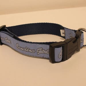 May include: A light blue dog collar with a black buckle and a silver ring. The collar has the text "Carolina Girl" printed on it in white.