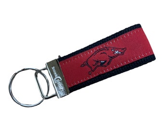 Puede incluir: Llavero rojo y negro con cierre y llavero de metal plateado. La tela roja presenta un logotipo de Razorback. La pulsera mide aproximadamente 15 cm de largo.
