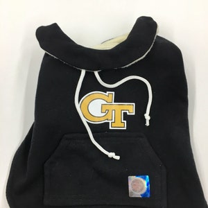 May include: Black dog hoodie with a white hood and a gold "GT" logo on the front. The hoodie has a white drawstring and a pocket on the front.