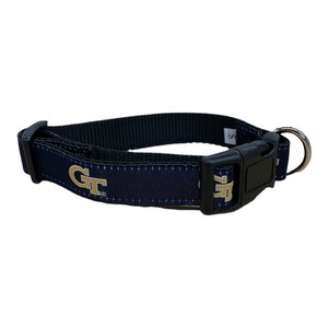 May include: A navy blue dog collar with a gold "GT" logo. The collar has a black plastic buckle and a silver metal D-ring.