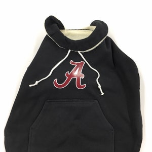 May include: Black hooded dog sweater with a red "A" on the front. The sweater has a white drawstring and a pocket.